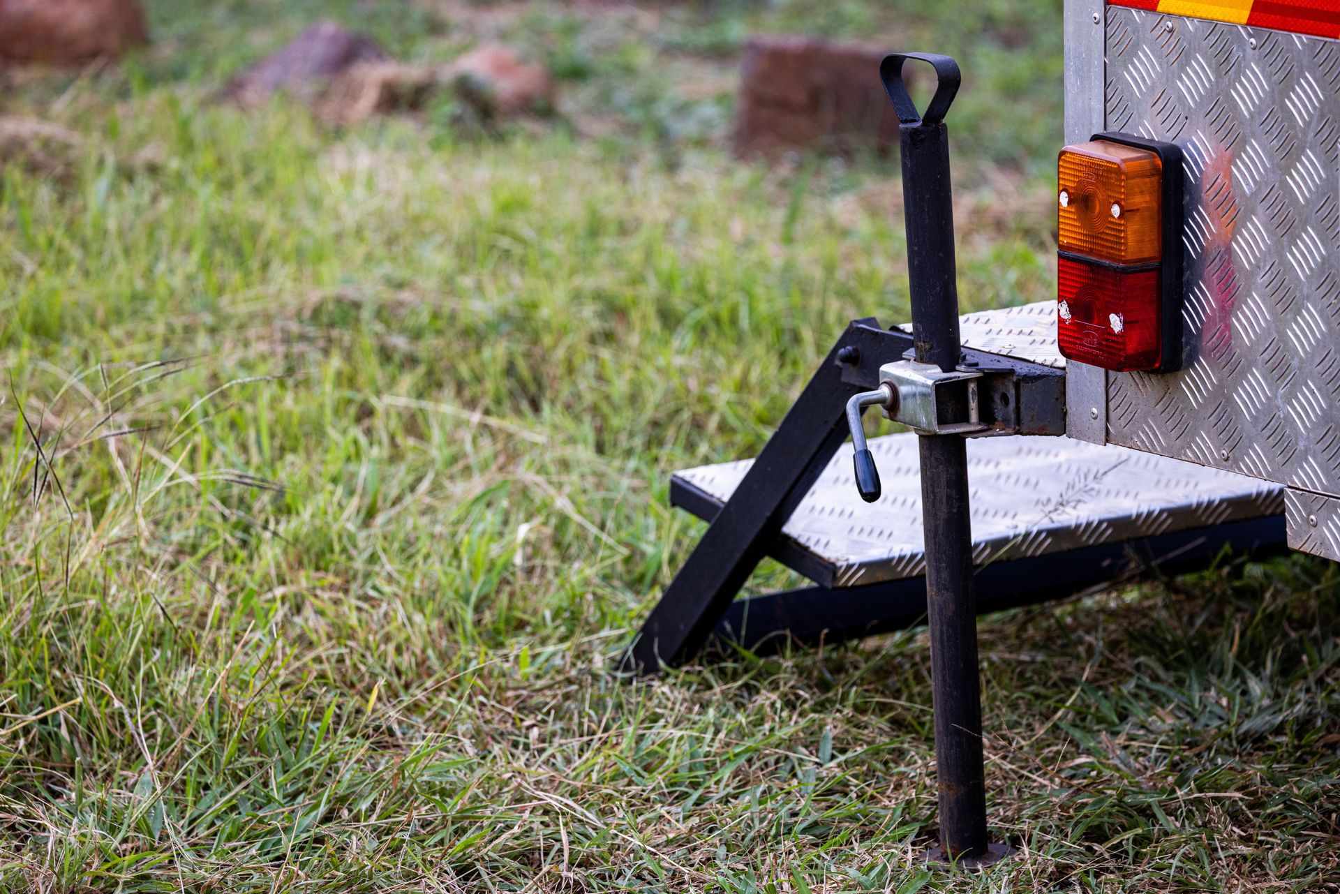Close-up of a trailer hitch and jack on metal steps in a grassy field, ideal for outdoor or camping themes.